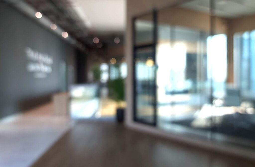 Blurred view of an office hallway with glass walls and modern décor, representing the experience of blurry vision caused by eye issues such as dryness.