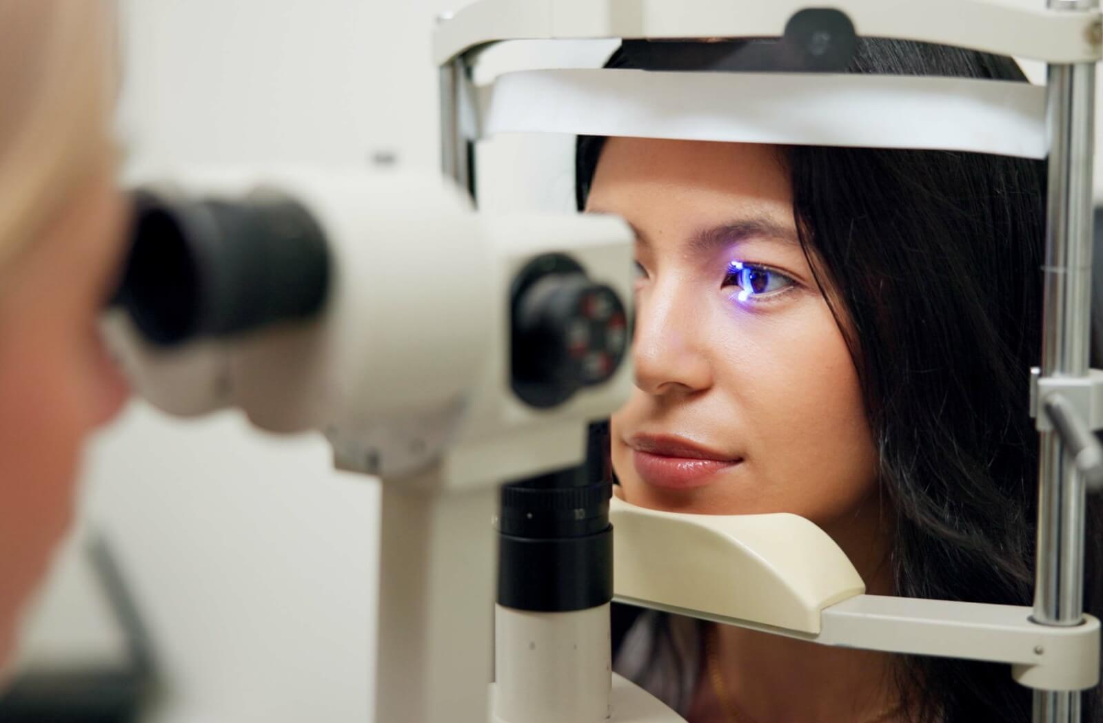 Close-up of a woman undergoing an eye exam with a slit lamp, as the optometrist examines her eye using a focused blue light to check eye health.