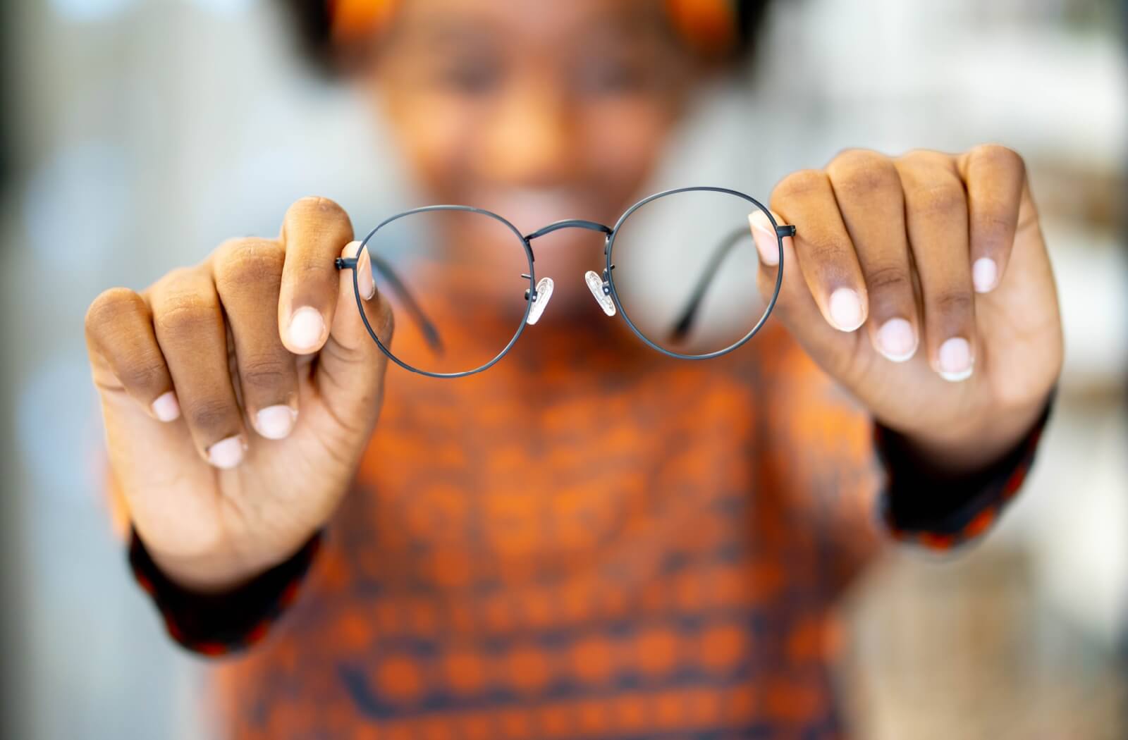 Hands holding up a pair of circular eyeglass frames.